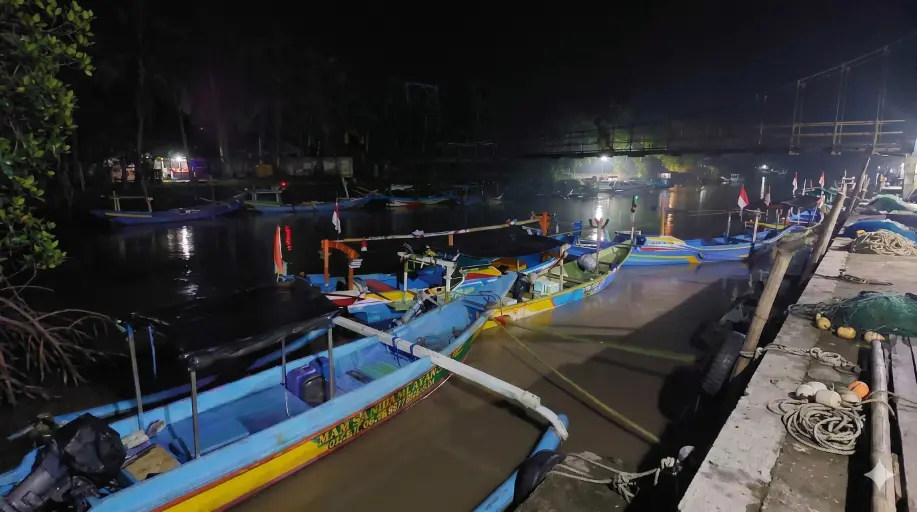 Barisan perahu nelayan tradisional dengan katir tertambat di dermaga Taman Nasional Alas Purwo pada malam hari.