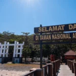 Pemandangan dari dermaga kayu Resor Sembulungan dengan papan tanda selamat datang kayu berukir dan gerbang masuk tradisional ke Taman Nasional Alas Purwo, Jawa Timur, Indonesia.