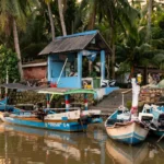 Perahu nelayan tradisional berlabuh di dermaga dekat pos penjaga Resor Tanjung Pasir dengan latar belakang pohon kelapa saat matahari terbenam.
