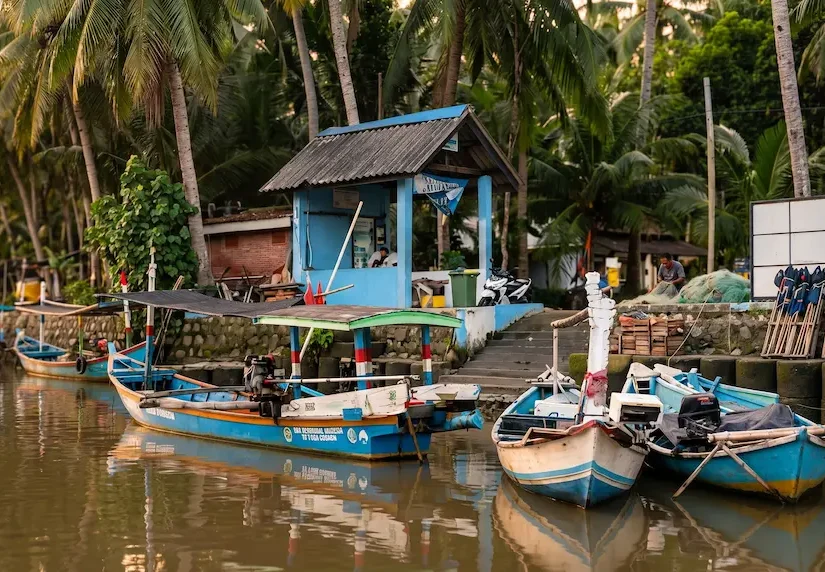 Perahu nelayan tradisional berlabuh di dermaga dekat pos penjaga Resor Tanjung Pasir dengan latar belakang pohon kelapa saat matahari terbenam.