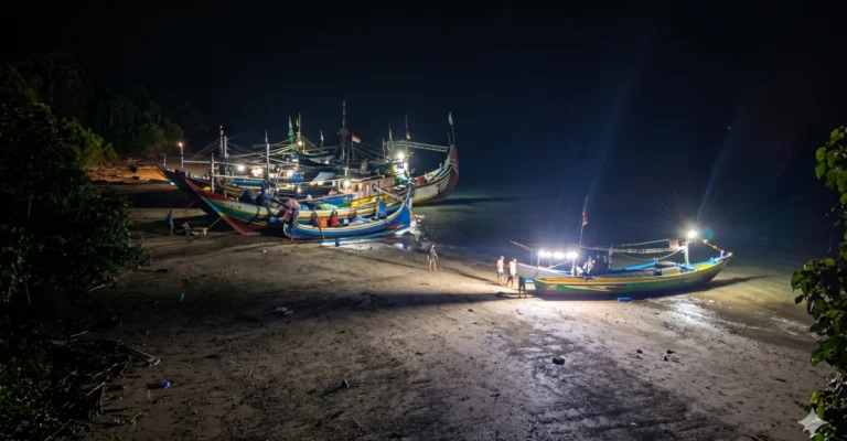 Sembilan unit kapal nelayan asal Muncar sedang bersandar dan melakukan perbaikan di pinggir pantai Resor Sembulungan pada malam hari dengan pencahayaan lampu kapal.