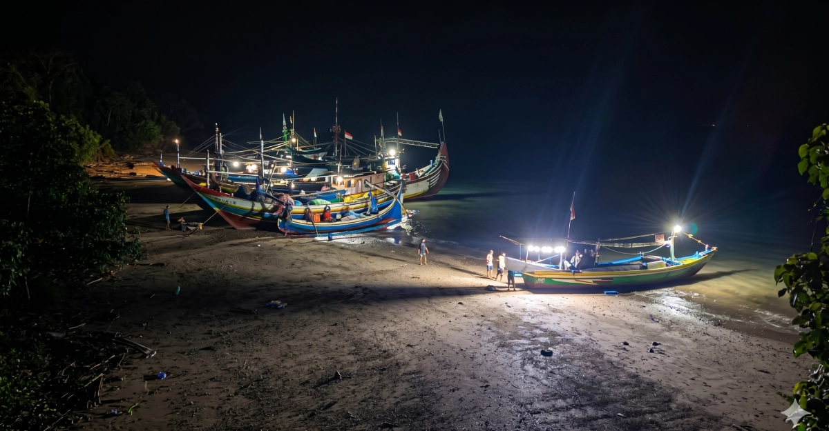 Sembilan unit kapal nelayan asal Muncar sedang bersandar dan melakukan perbaikan di pinggir pantai Resor Sembulungan pada malam hari dengan pencahayaan lampu kapal.