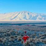 Tim pemadam kebakaran gabungan berseragam merah dari BKO TN Alas Purwo berjalan membawa peralatan melintasi savana yang hangus terbakar di Taman Nasional Bromo Tengger Semeru dengan latar belakang gunung.